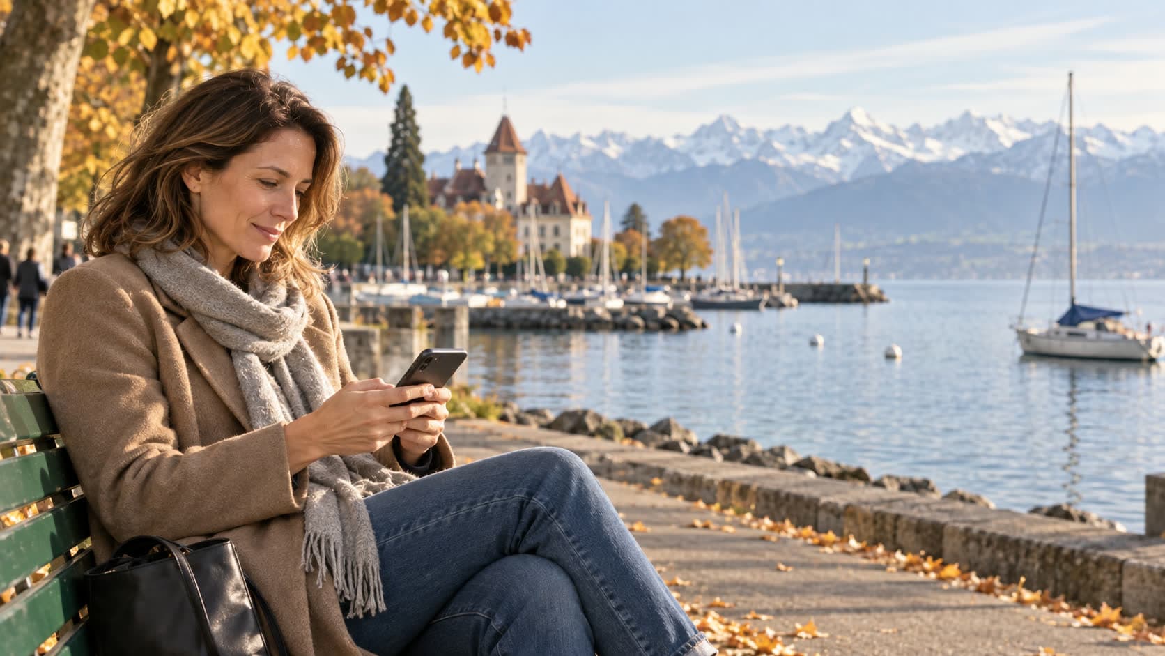 Une femme consulte son téléphone sur un banc au bord du Léman à Ouchy, avec les Alpes en arrière-plan