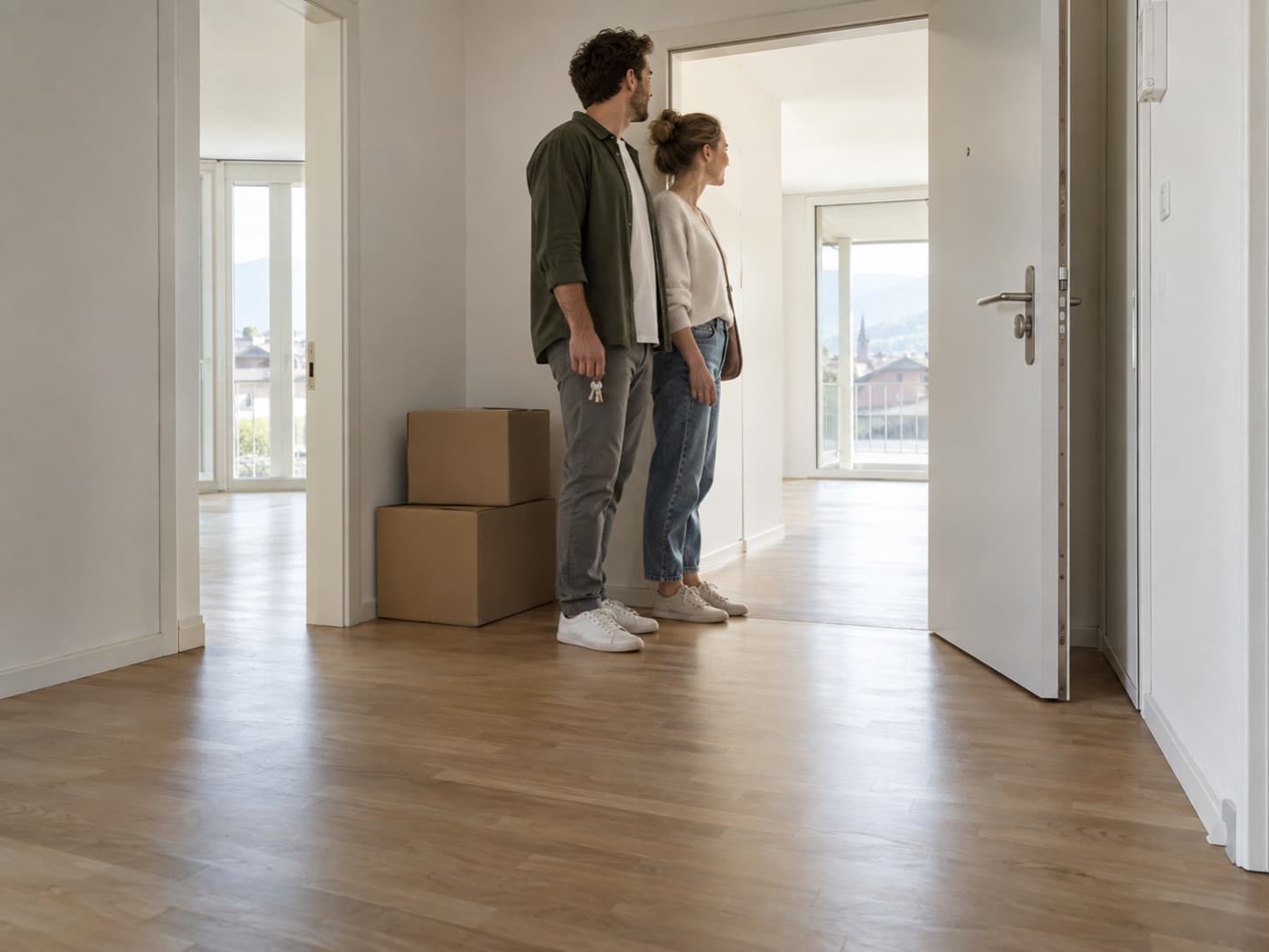 Un couple d’une trentaine d’années devant la porte d’un appartement, un trousseau de clés à la main, des cartons derrière eux.