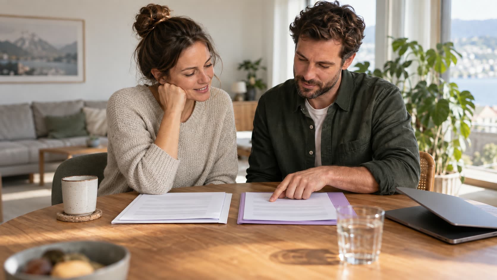 Un couple compare deux dossiers posés côte à côte sur la table du salon, l’un blanc, l’autre lilas