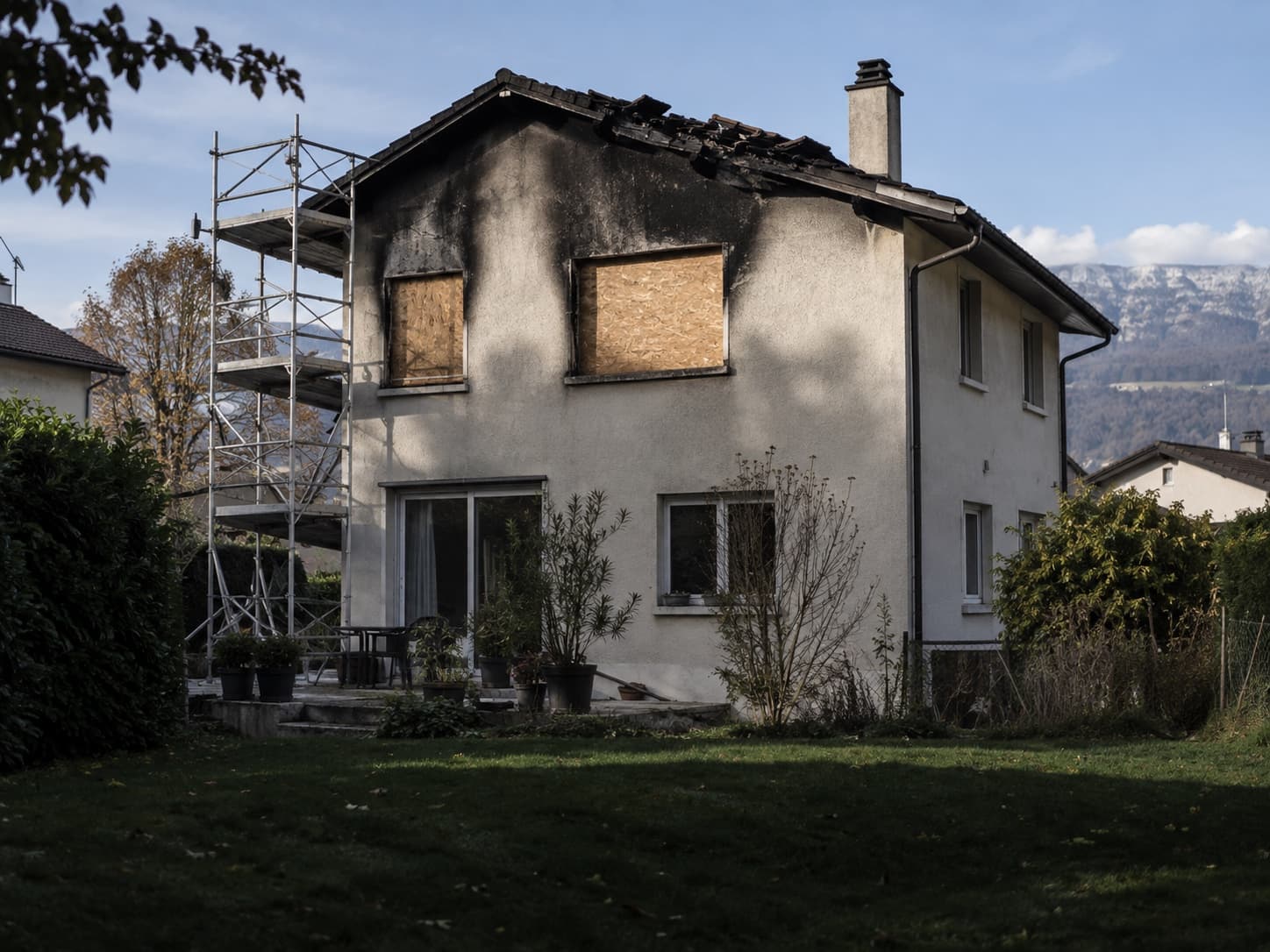 Une maison à la façade et à la toiture noircies, avec deux fenêtres condamnées par des panneaux de bois et un échafaudage sur le côté.