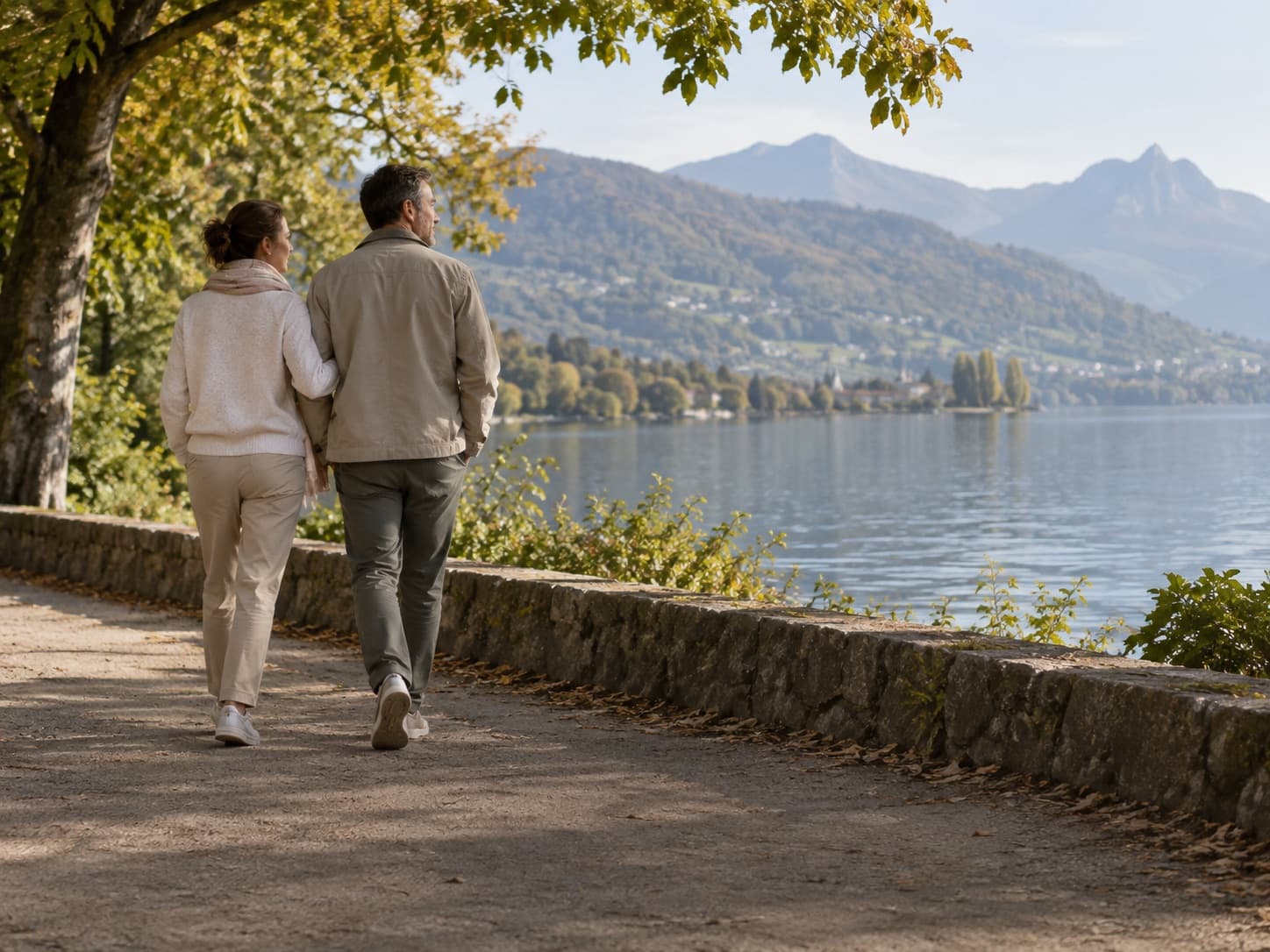 Un couple d’une quarantaine d’années marche côte à côte sur un chemin au bord d’un lac, elle tient son bras.